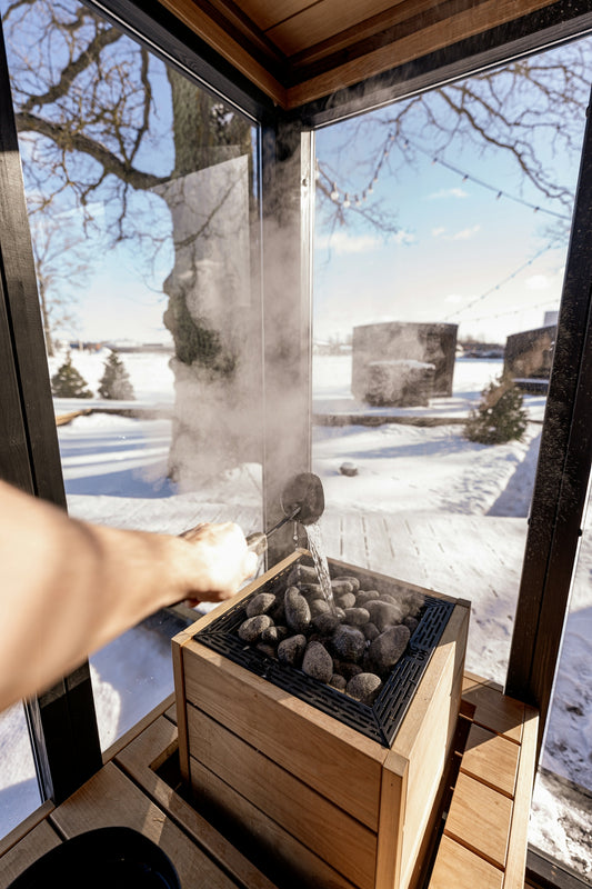 Man pours water on sauna rocks, creating steam